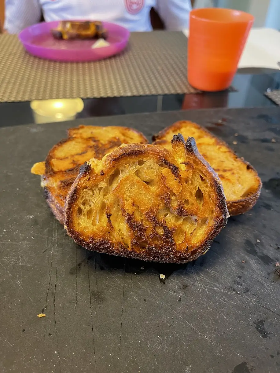 Thick slices of sourdough with dark grill char across the crust, cooling on a dark kitchen counter