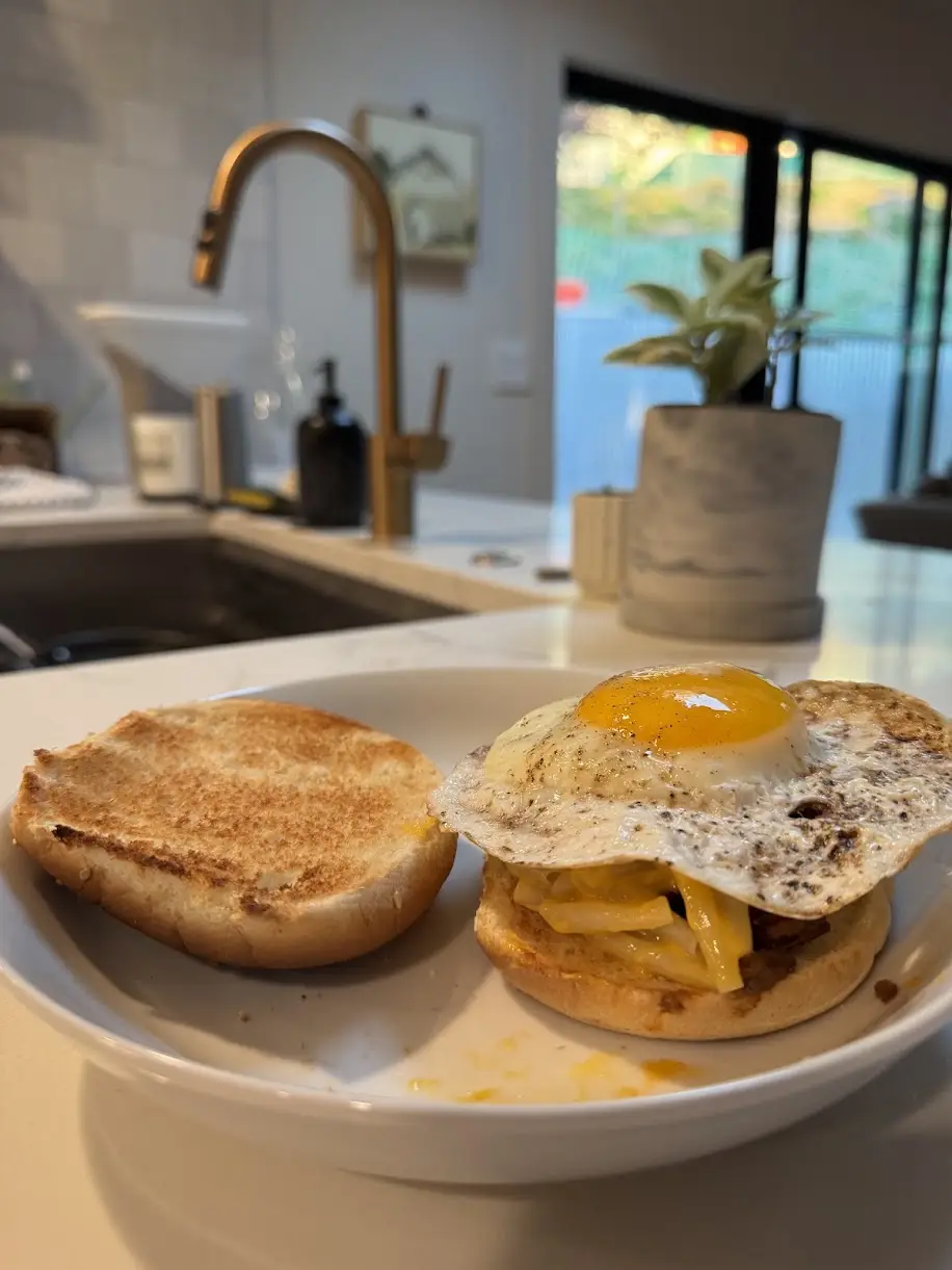 A toasted English muffin breakfast sandwich with cheese, bacon and a fried egg with crisp lacy edges