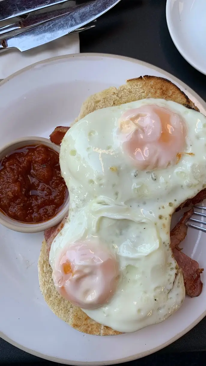 Two sunny side up eggs over bacon on toasted bread with a small ramekin of tomato chutney