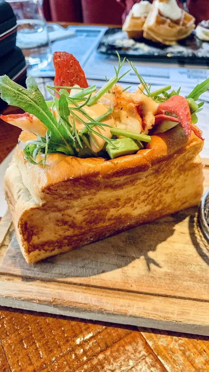 A hollowed block of toasted milk bread filled with lobster, avocado and arugula, on a wooden board